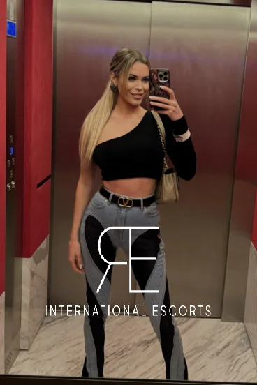 Selfie of blonde London escort Rizzo wearing a black top and stone washed jeans 