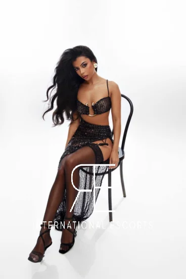 Elegant and expensive escort Mannu is sitting on a black chair 