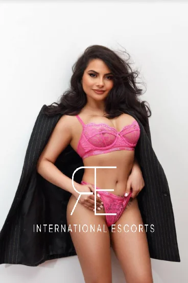 Busty Brazilian escort Gabby wearing pink lingerie with a black blazer over her shoulders 