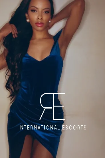 Ebony London escort wearing a blue dress and has her hands above her head 